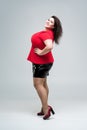 Happy plus size fashion model in red blouse and black skirt, fat woman on gray background, body positive concept Royalty Free Stock Photo