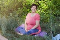 Happy plus size girl in fitness uniform sitting on meditation mat in nature. Copyspace Royalty Free Stock Photo