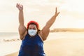 Happy plus size woman walking on the beach while wearing face mask - Curvy overweight model having fun during vacation