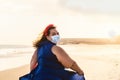 Happy plus size woman walking on the beach while wearing face mask - Curvy overweight model having fun during vacation