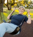 Happy portrait of American senior mature beautiful woman on her 70s sitting on park swing outdoors relaxed smiling and having fun Royalty Free Stock Photo