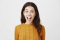 Happy positive european dark-haired female with pierced nose in trendy yellow sweater standing with opened mouth over