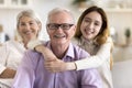 Happy positive grandfather posing at camera with hugging teenage grandkid