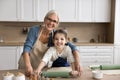 Happy positive grandma teaching cute grandchild in apron to bake