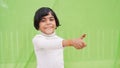 Happy positive little girl in white turtleneck showing thumb up like gesture isolated on plain pastel light green color background Royalty Free Stock Photo