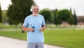 Happy positive mature man with broad smile holding water bottle while doing sport in city park