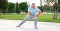 Happy positive mature sportsman in headphones doing side squat during outdoor workout
