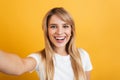 Happy positive pleased young blonde woman posing isolated over yellow wall background dressed in white casual t-shirt take selfie Royalty Free Stock Photo