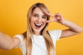 Happy positive pleased young blonde woman posing isolated over yellow wall background dressed in white casual t-shirt take selfie Royalty Free Stock Photo