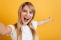 Happy positive pleased young blonde woman posing isolated over yellow wall background dressed in white casual t-shirt take selfie Royalty Free Stock Photo