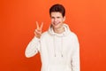 Happy positive teenager in stylish sweatshirt showing v sign to camera, winking and smiling, young man wishing good luck, peace