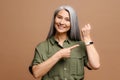 Happy positive woman with grey hair in pointing finger on watch on her wrist looking at camera with toothy smile. Look Royalty Free Stock Photo