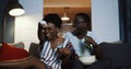 Happy positive young African man and woman smile and talk watching TV, using remote at home with snacks slow motion.