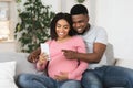 Happy pregnant black couple using smartphone together at home Royalty Free Stock Photo