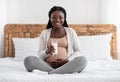 Happy Pregnant African Woman Drinking Milk While Sitting On Bed At Home Royalty Free Stock Photo