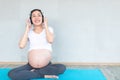 Happy pregnant asian woman applying headphones to her belly for prenatal music stimulation. Music and Emotion Concept.