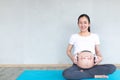 Happy pregnant asian woman applying headphones to her belly for prenatal music stimulation. Music and Emotion Concept.