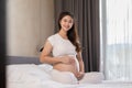 Happy Pregnant Asian Woman sitting on bed holding and stroking her big belly at home,Pregnancy of young woman enjoying with future