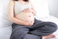 Happy pregnant asian woman sitting on bed and touching her big belly