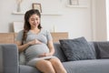 Happy Pregnant Asian Woman sitting on sofa holding and stroking her big belly at home,Pregnancy of young woman enjoying with Royalty Free Stock Photo