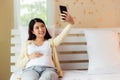 Happy pregnant asian woman taking selfie on smartphone in bed at home or Young asia pregnancy mother showing big abdomen to her Royalty Free Stock Photo