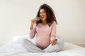 Happy pregnant black woman enjoying chocolate while sitting on bed at home Royalty Free Stock Photo