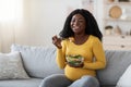 Happy pregnant black woman sitting on couch, eating fresh salad Royalty Free Stock Photo