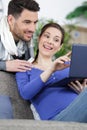 happy pregnant couple slooking on laptop sat on couch
