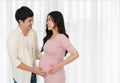 Happy pregnant couple stroking and talking with baby in belly on window background