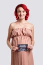 A happy pregnant girl is holding a picture of an ultra sound study. White background.