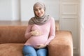 Happy Pregnant Muslim Woman Posing Hugging Belly Sitting At Home