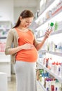 Happy pregnant woman choosing lotion at pharmacy