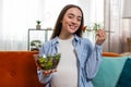 Happy pregnant woman with great appetite eats vegetable salad sitting on sofa healthy food self-care Royalty Free Stock Photo