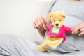 Happy pregnant woman hand holding teddy bear doll on her belly w Royalty Free Stock Photo