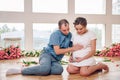 Happy pregnant woman with her husband are holding and listening to baby in belly and setting on living room`s floor at home, preg Royalty Free Stock Photo
