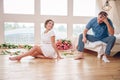 Happy pregnant woman with her husband are holding and listening to baby in belly and setting on living room`s floor at home, preg Royalty Free Stock Photo