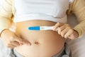 Happy pregnant woman holding pregnancy test pointing finger to beautiful belly that pregnant girl has fetus inside. Young Mother