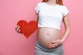 Happy pregnant woman holding red heart near the belly, on a pink background Royalty Free Stock Photo