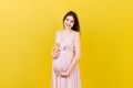 Happy pregnant woman holding a teddy bear against her belly at Colored background. Young mother is expecting a baby Royalty Free Stock Photo