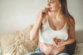 Happy pregnant woman at home eating fresh nuts - almonds, walnuts. Healthy pregnancy concept