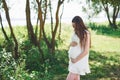 Happy pregnant woman hugging her stomach on the background of park, outdoor Royalty Free Stock Photo