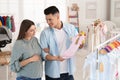 Happy pregnant woman with husband choosing baby clothes in store. Shopping concept Royalty Free Stock Photo