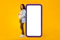Happy pregnant woman leaning at big smartphone with blank screen and embracing her belly, advertising pregnancy app