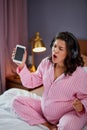 Happy pregnant woman listen to music with headphones while sitting on the bed at home Royalty Free Stock Photo