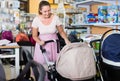 happy pregnant woman looking for baby carriage at kids shop