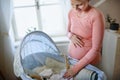 Happy pregnant woman looking at little clothes for her baby in cradle.