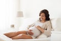 Happy pregnant woman lying on bed at home