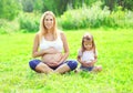 Happy pregnant woman, mother and little daughter child sitting on grass doing yoga exercise in summer Royalty Free Stock Photo