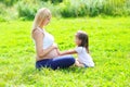 Happy pregnant woman, mother and little daughter child sitting on grass in summer Royalty Free Stock Photo