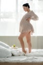 Happy pregnant woman in nightie touching tummy while standing on bed Royalty Free Stock Photo